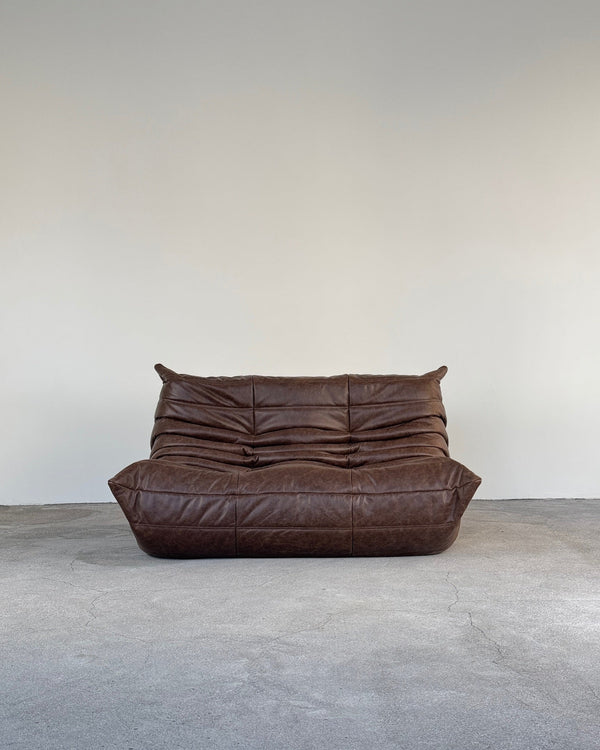 Brown leather togo sofa on a gray floor with a white wall background