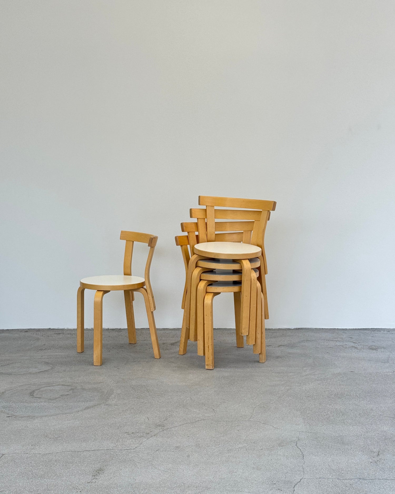 Stack of wooden stools against a light gray wall.