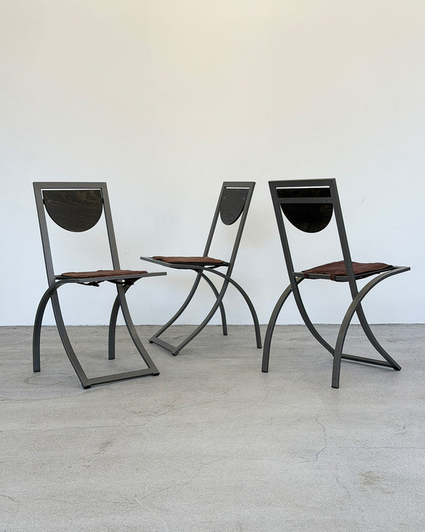 Three modern chairs with metal frames and brown seats on a light wooden floor.