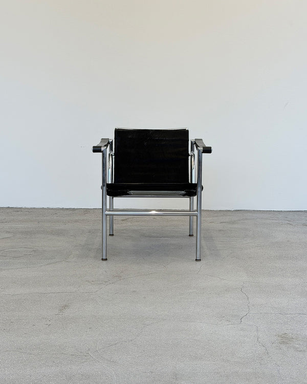 Black Le Corbusier LC1 chair with metal frame on a light wooden floor against a white wall