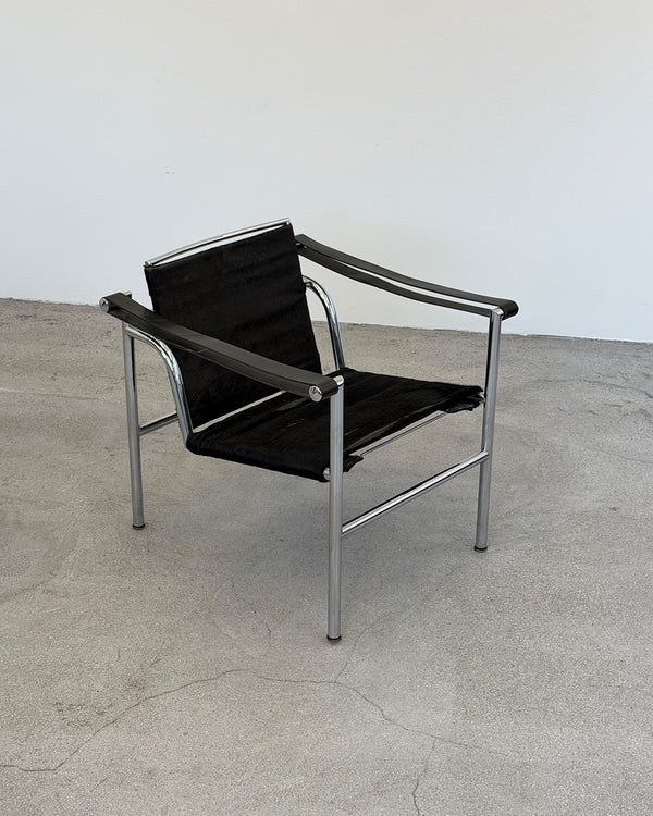 Modern Le Corbusier LC1 chair with black leather seat and silver frame on a concrete floor.