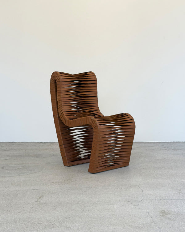 Brown wavy chair on a light wooden floor with a white wall background