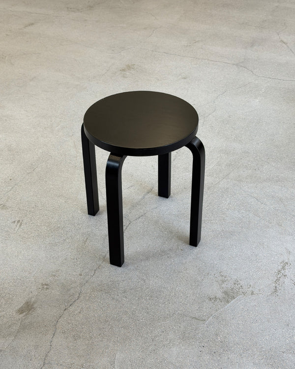 Black Artek E60 stool on a gray concrete floor
