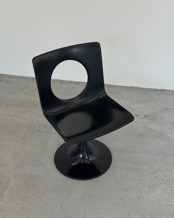 Black chair with a circular design on a gray floor and white wall