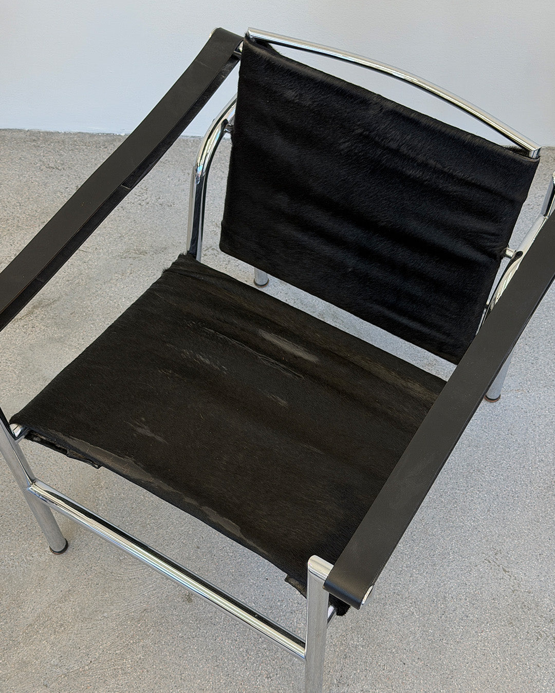 Black Le Corbusier LC1 chair with chrome frame on a gray floor