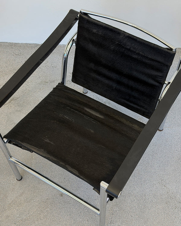 Black Le Corbusier LC1 chair with chrome frame on a gray floor