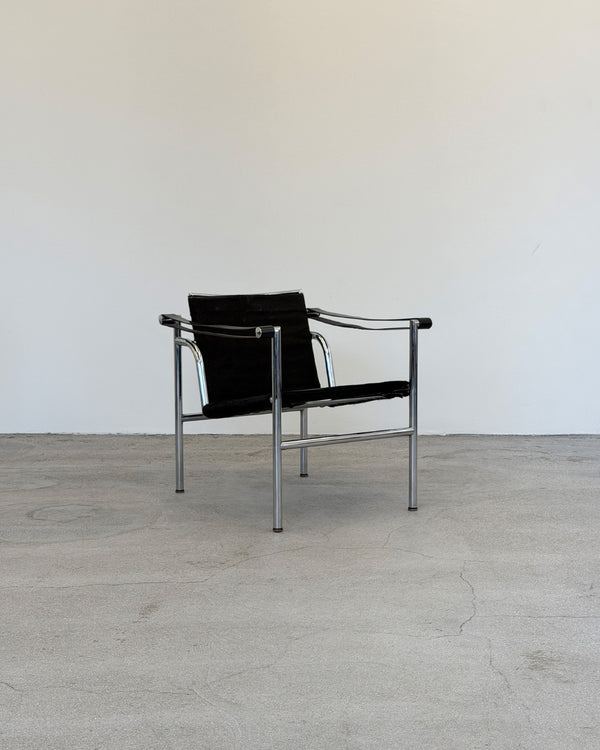 Black Le Corbusier LC1 chair with metal frame on a gray floor and white wall