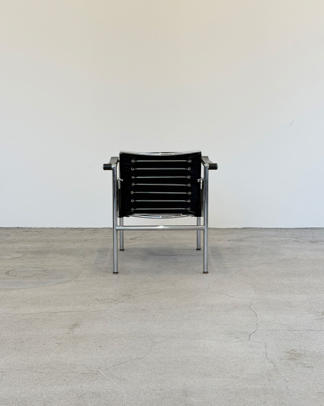 Black Le Corbusier LC1 chair with metal frame on a light wooden floor against a white wall