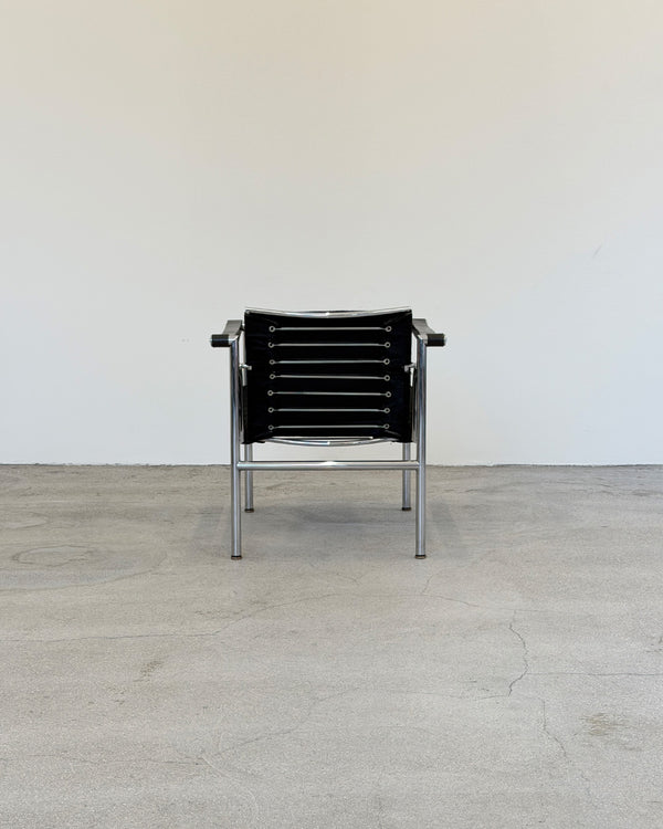 Black Le Corbusier LC1 chair with metal frame on a light wooden floor against a white wall