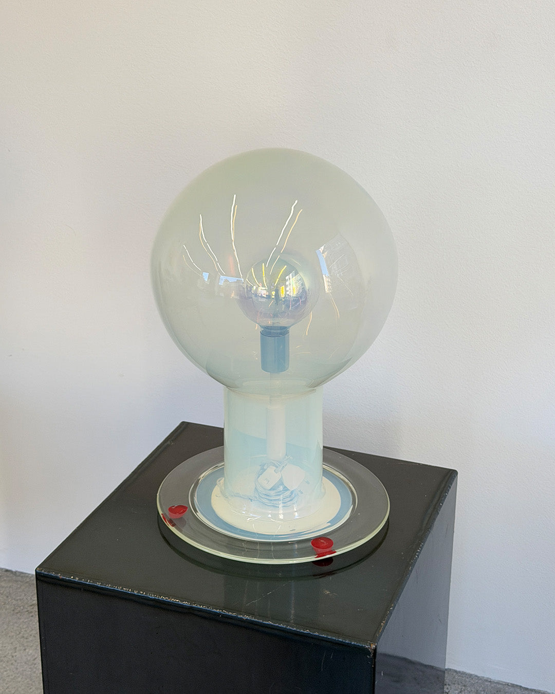 Large glass light bulb on a black pedestal against a white wall