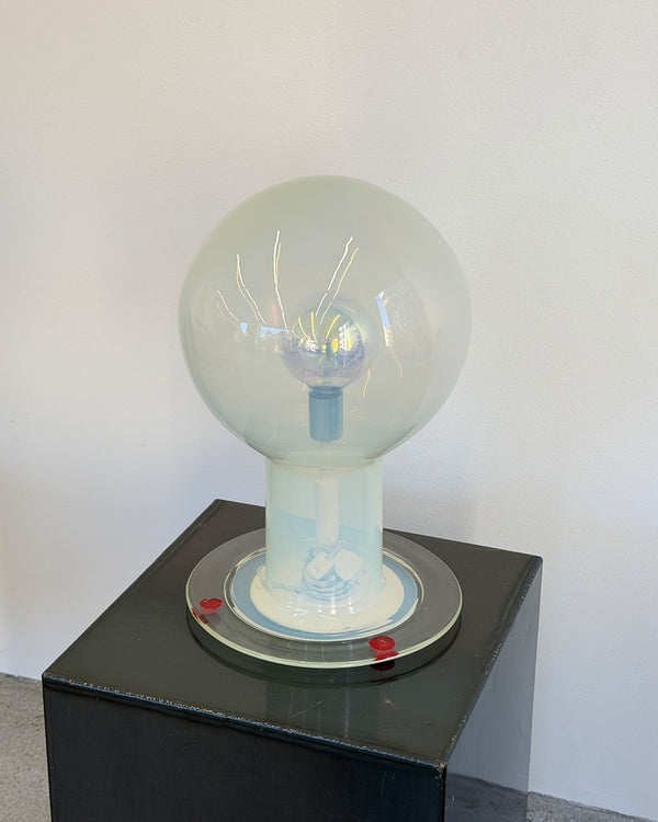 Large glass light bulb on a black pedestal against a white wall