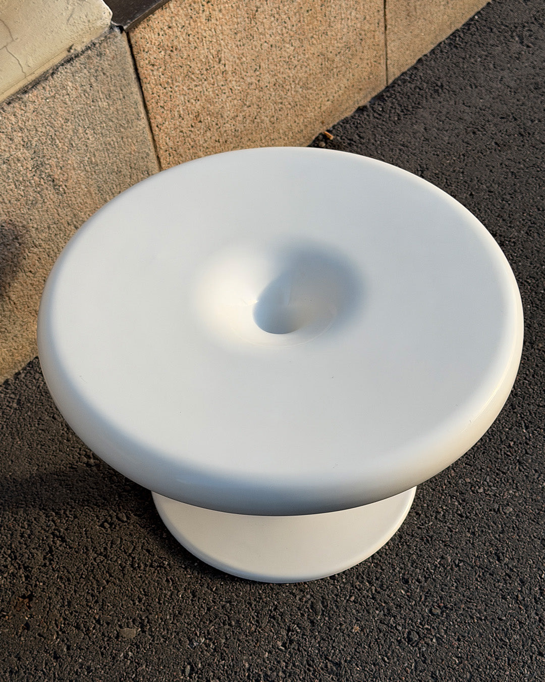 Round white Eero Aarnio Kanttarelli table on a textured surface