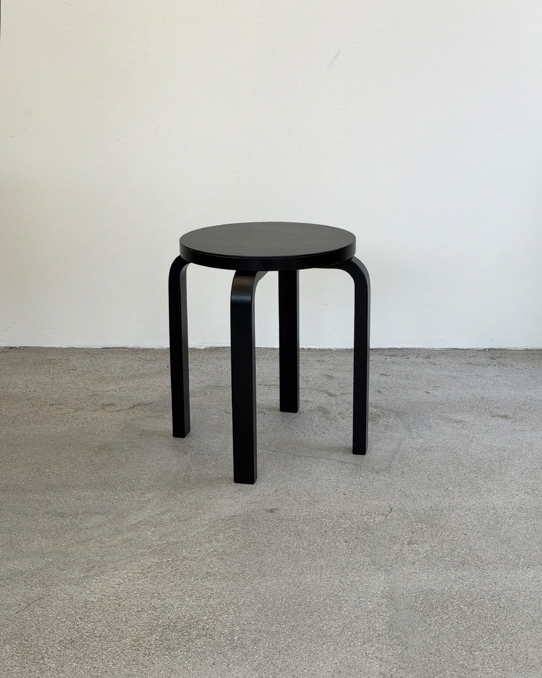 Black stool on a gray floor with a white wall background