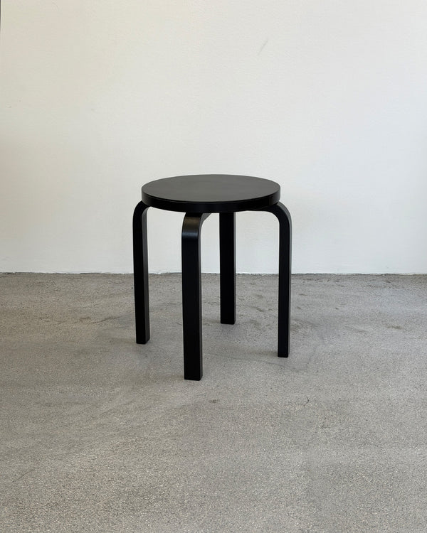 Black stool on a gray floor with a white wall background