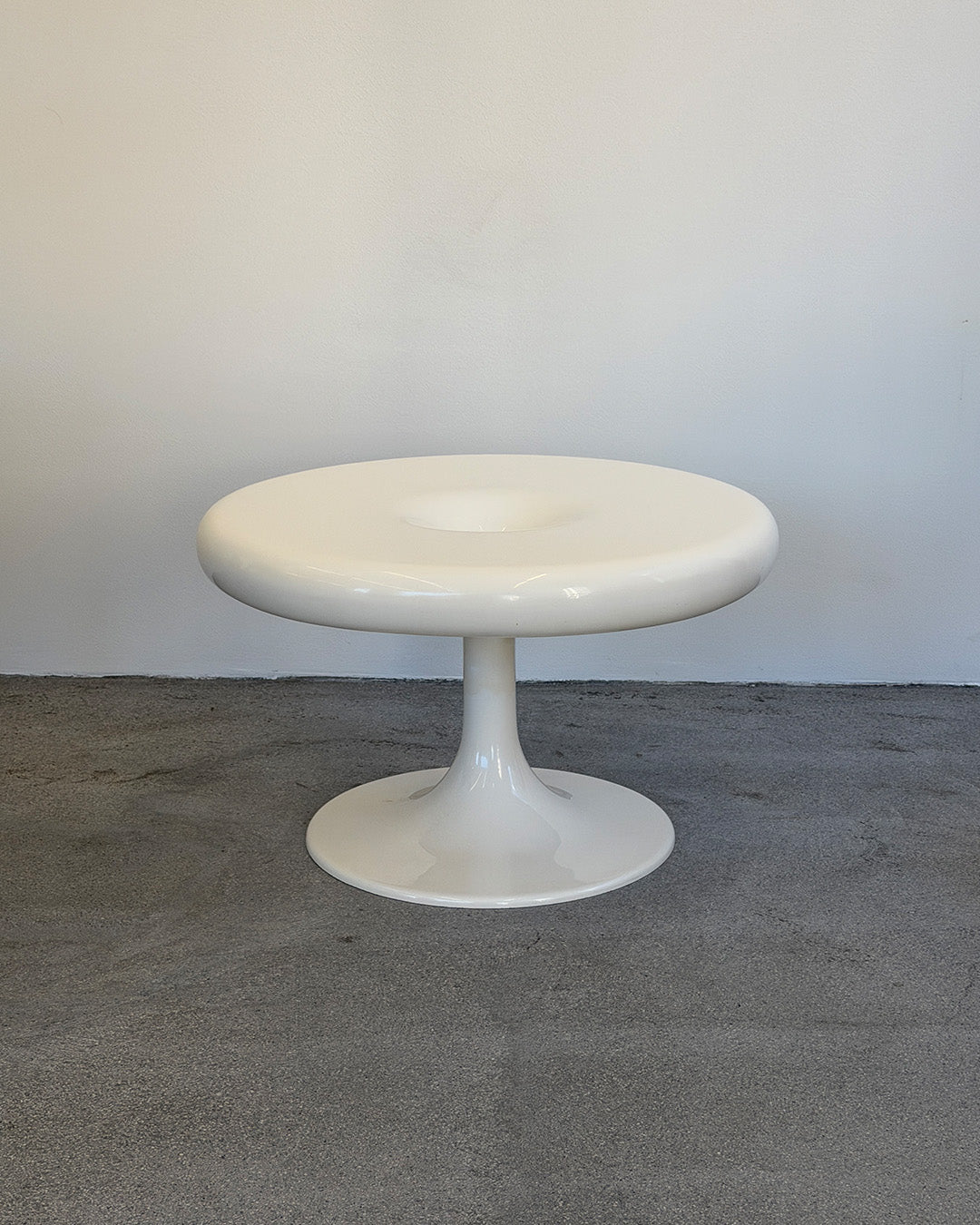 White Eero Aarnio Kanttarelli pedestal table on a gray floor with a white wall background
