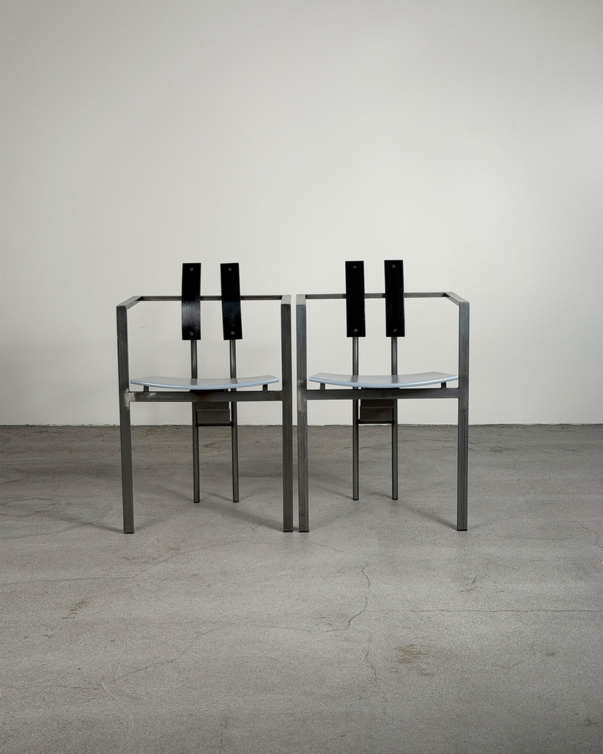 Two black chairs with glass seats on a gray floor and white wall background