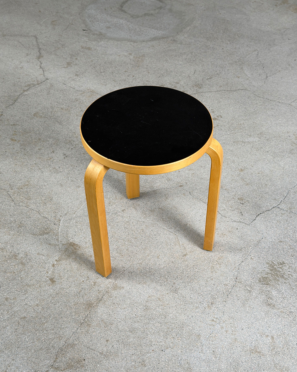 Black stool with wooden legs on a gray concrete floor