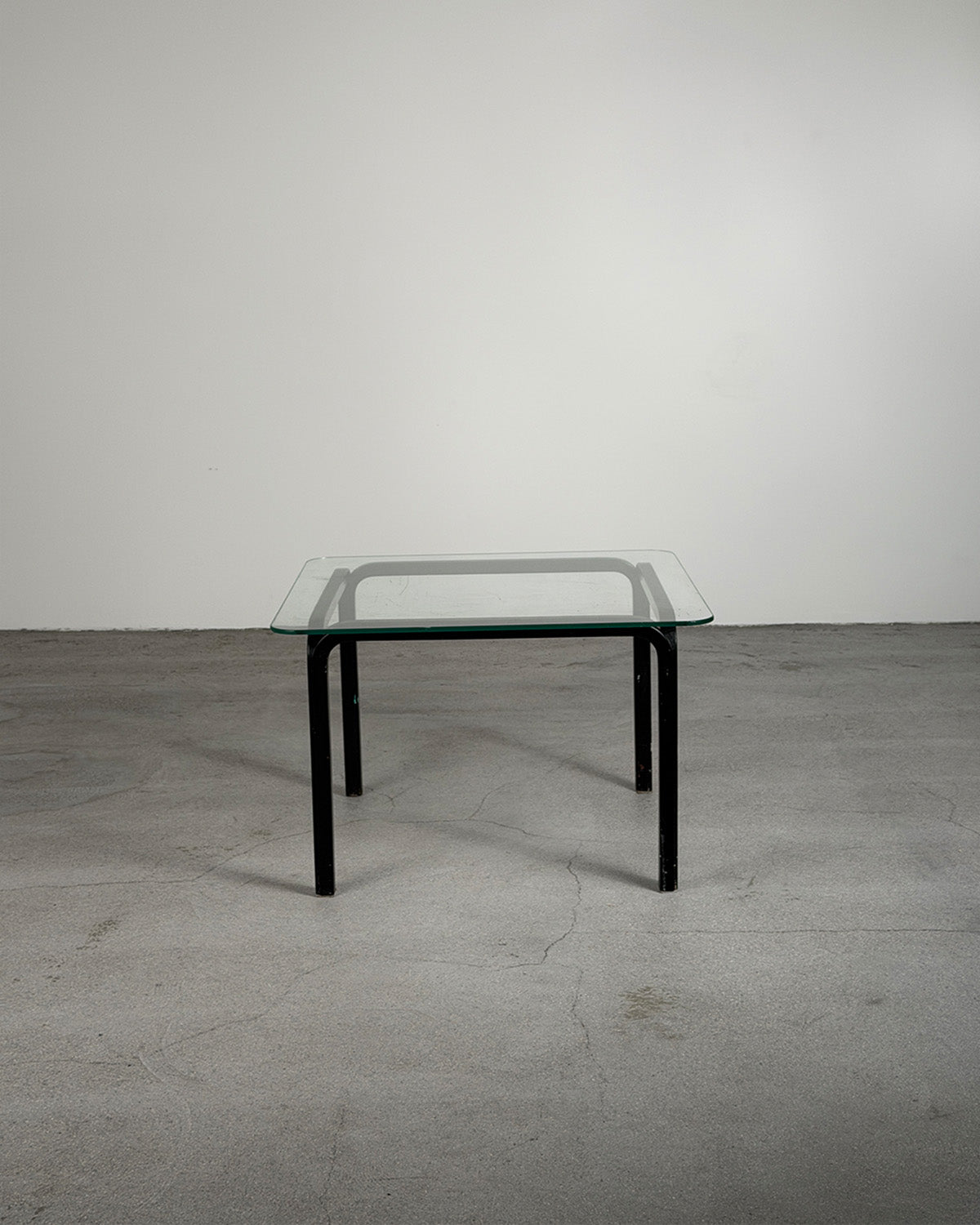 Glass table with black legs on a gray floor and white wall