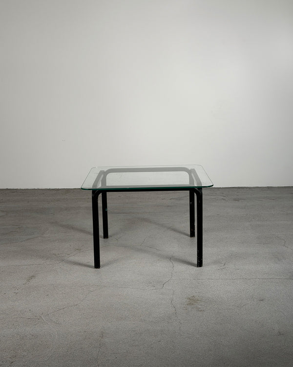 Glass table with black legs on a gray floor and white wall