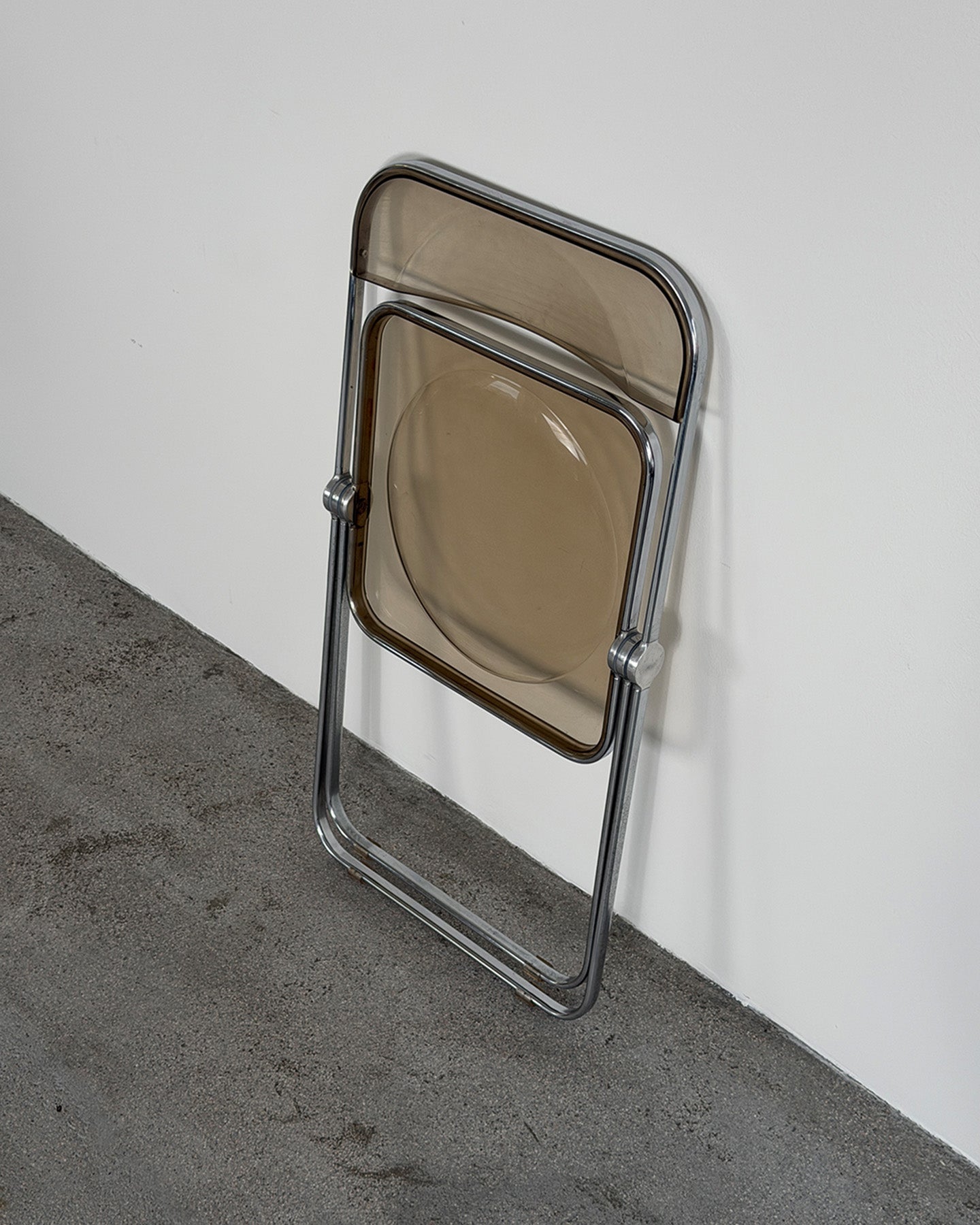 Foldable chair with smoked glass seat and backrest against a white wall.