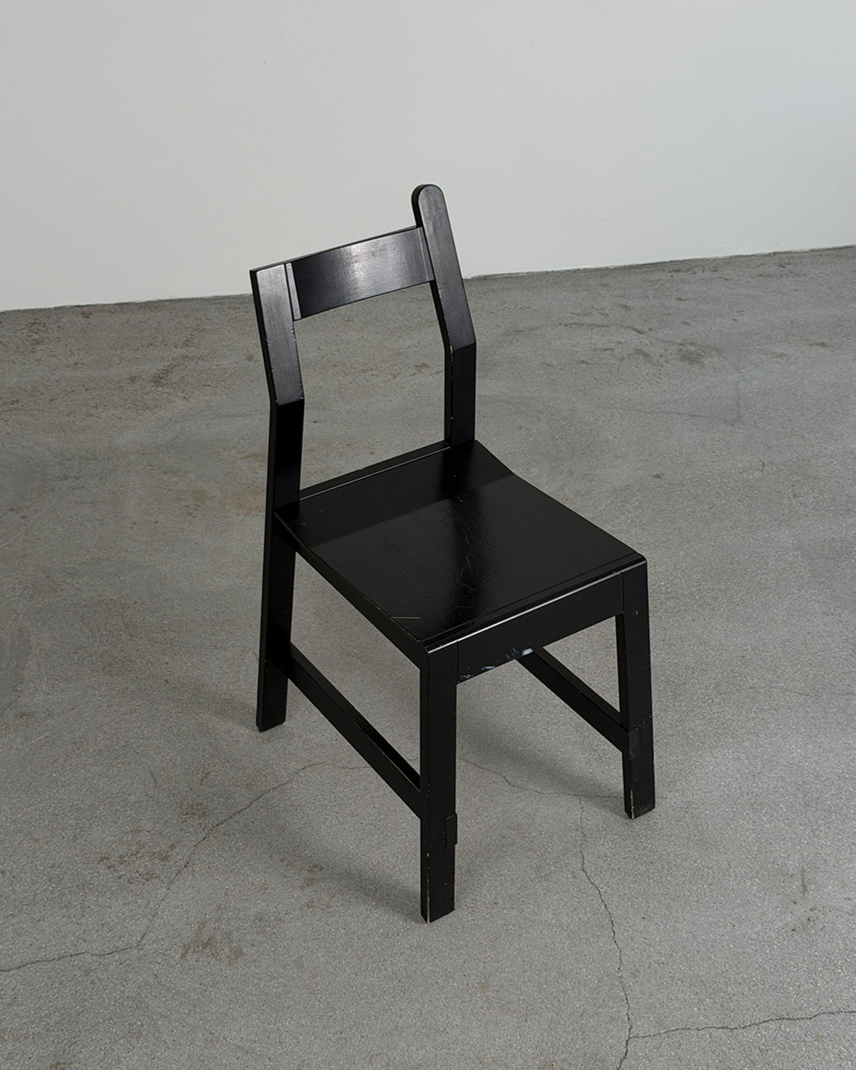 Black wooden chair on a gray concrete floor with a white wall background