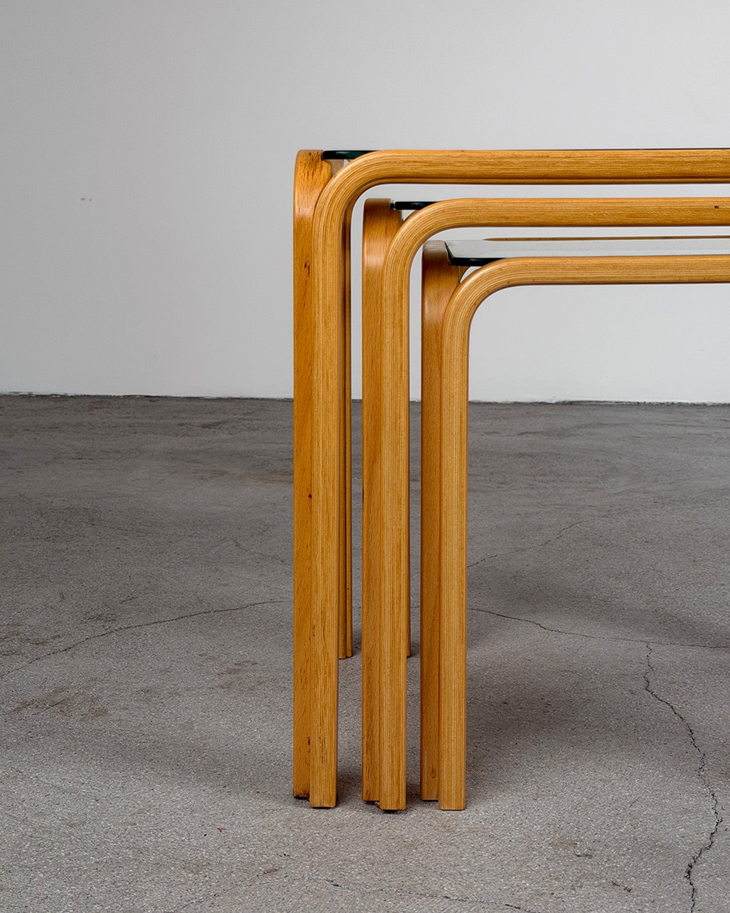 Three wooden nesting tables on a concrete floor with a gray background