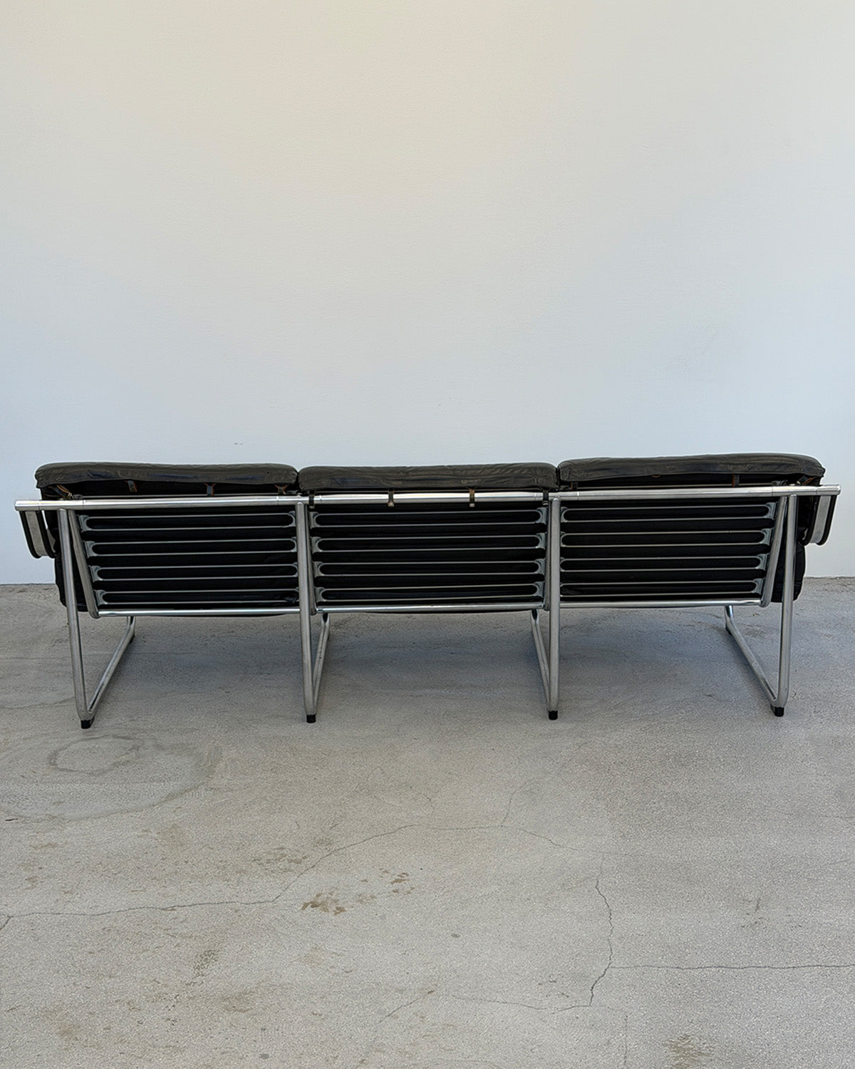 Modern black leather sofa with chrome frame on a light gray floor.