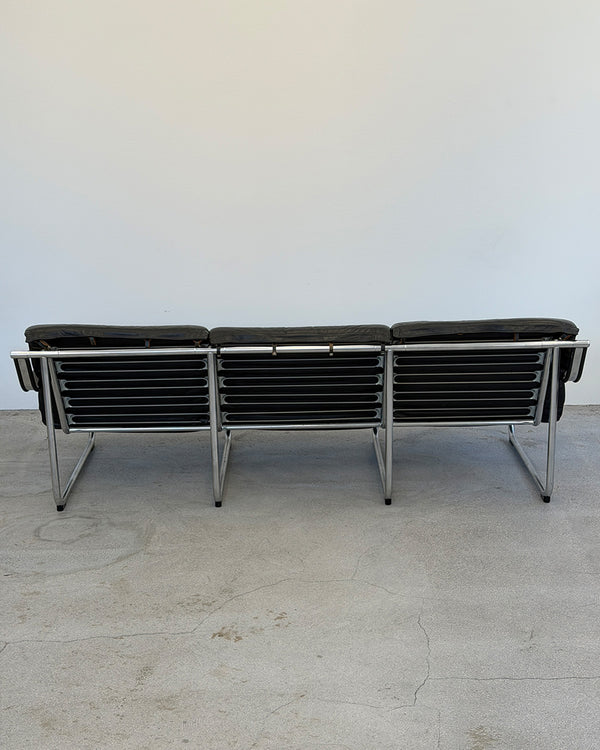 Modern black leather sofa with chrome frame on a light gray floor.