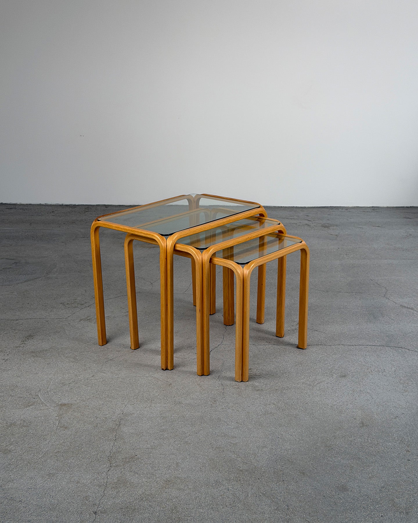 Set of three nesting tables with glass tops on a concrete floor.