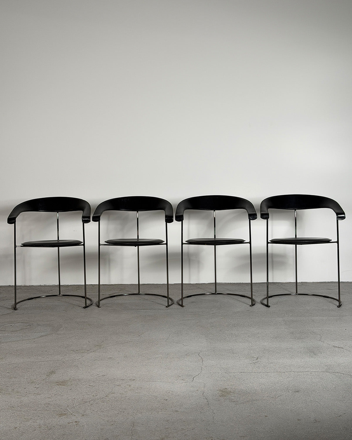 Four black chairs with metal legs on a gray floor and background