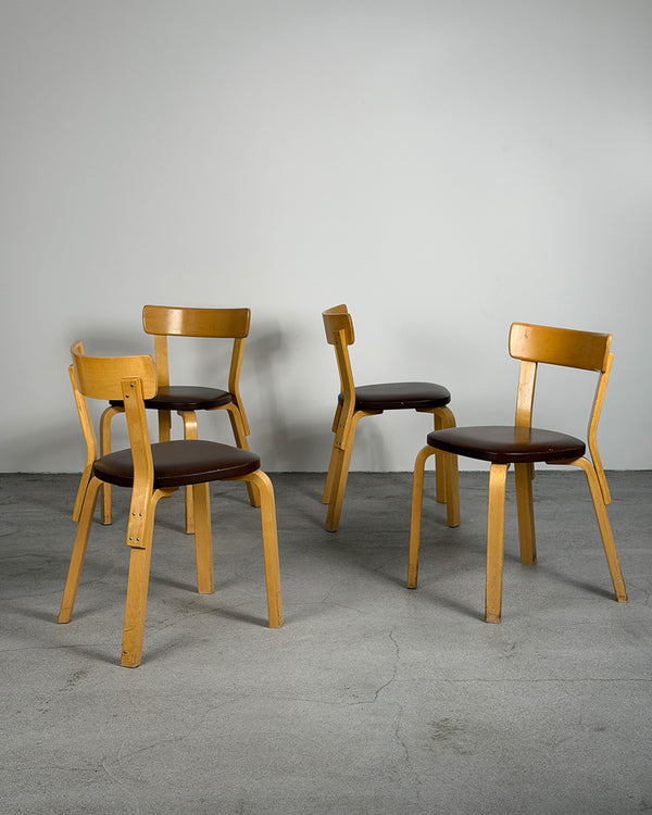 Four wooden chairs with brown seats on a gray floor and wall.