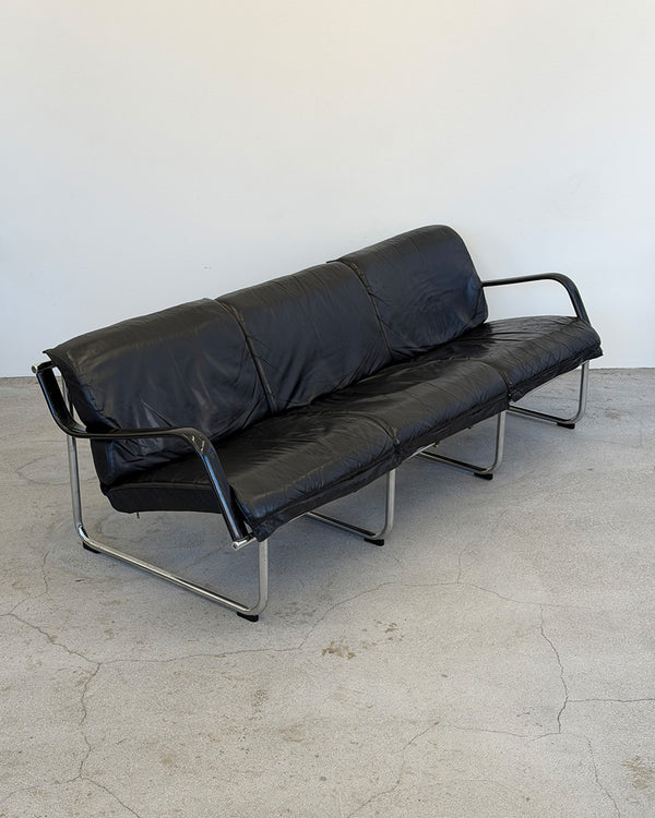 Black leather sofa with metal frame on a concrete floor against a white wall