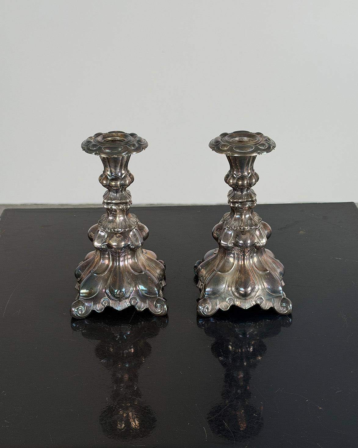 Two silver Kultakeskus candlestick holders on a reflective black surface with a light gray background