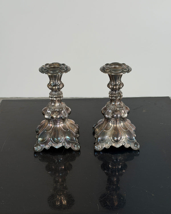 Two silver Kultakeskus candlestick holders on a reflective black surface with a light gray background