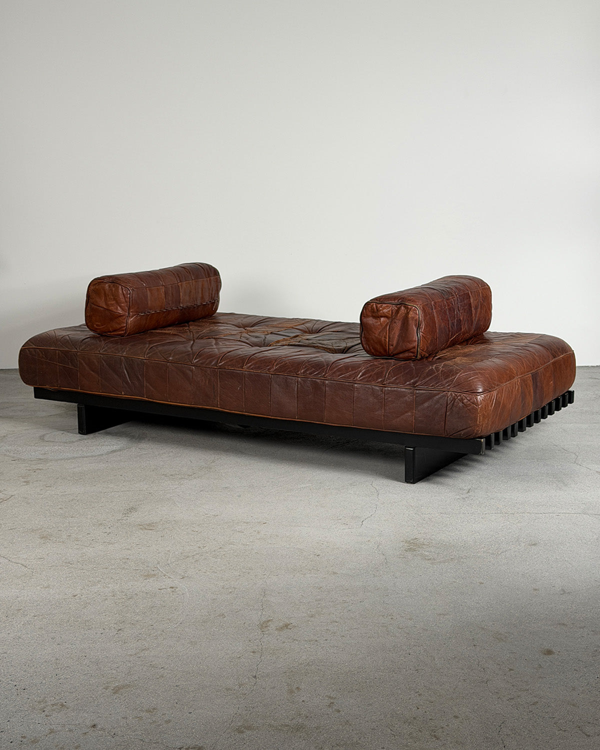 Brown leather sofa with cylindrical backrests on a plain floor.