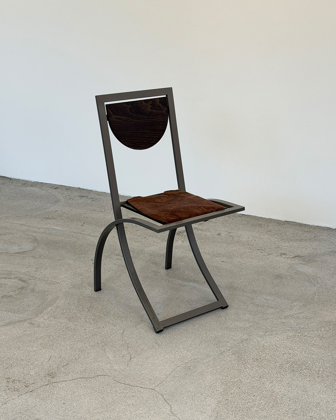 Chair with wooden seat and backrest on a concrete floor with white wall background