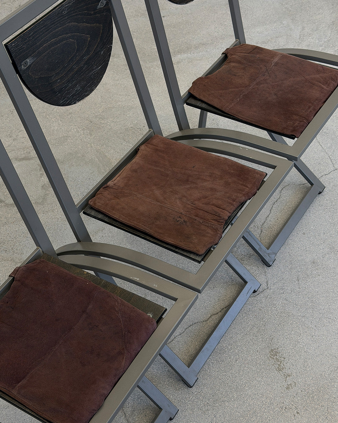 Three metal chairs with brown cushioned seats on a concrete floor.
