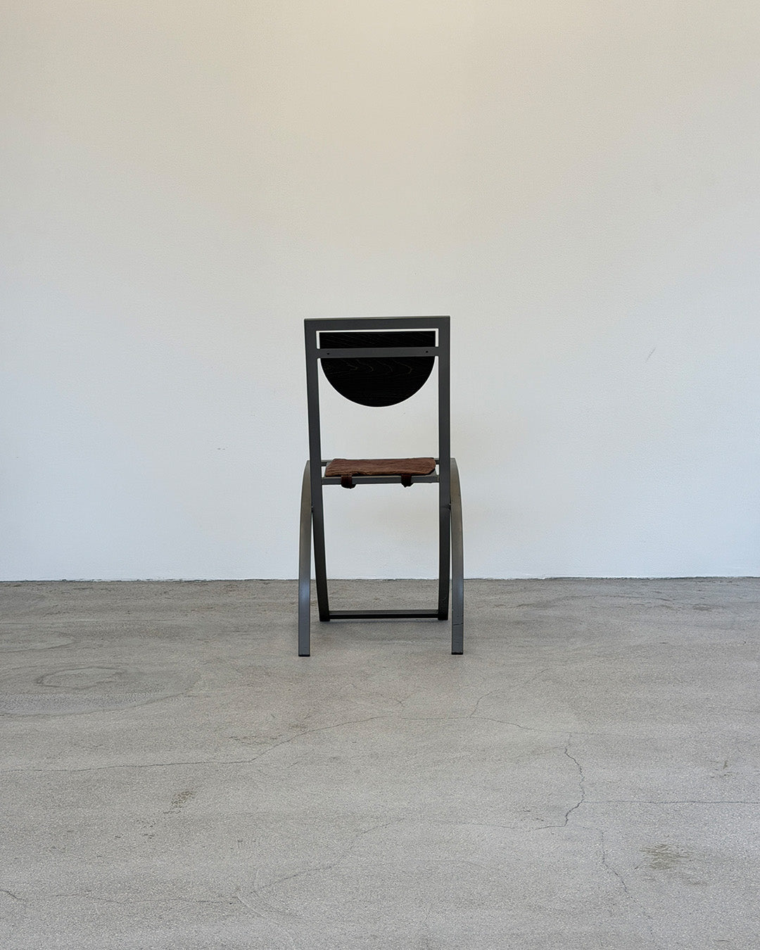 Chair with black frame and wooden seat on a gray floor against a white wall