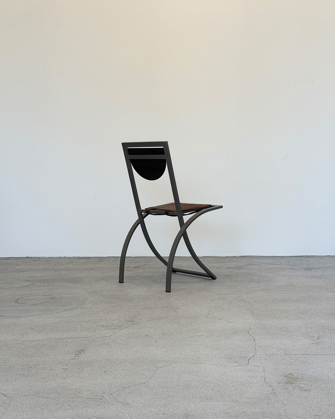 Black metal chair with a brown seat on a gray floor against a white wall