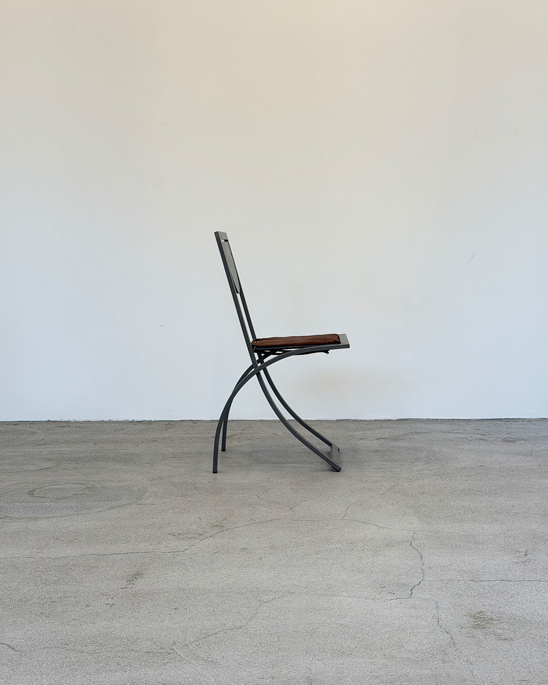 Vintage chair with metal frame and wooden seat on a plain floor and white wall background