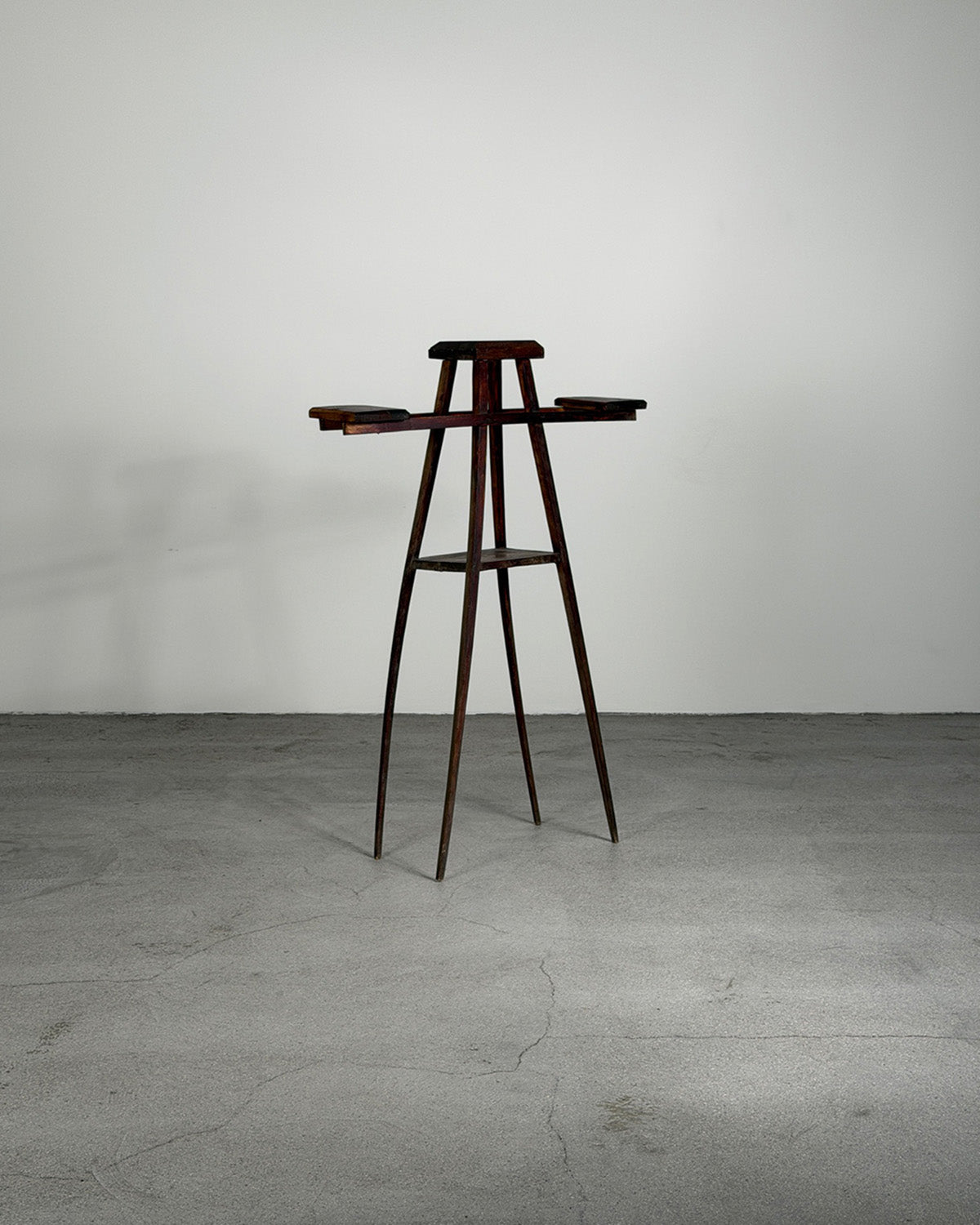 Wooden bar stool against a plain wall on a gray floor