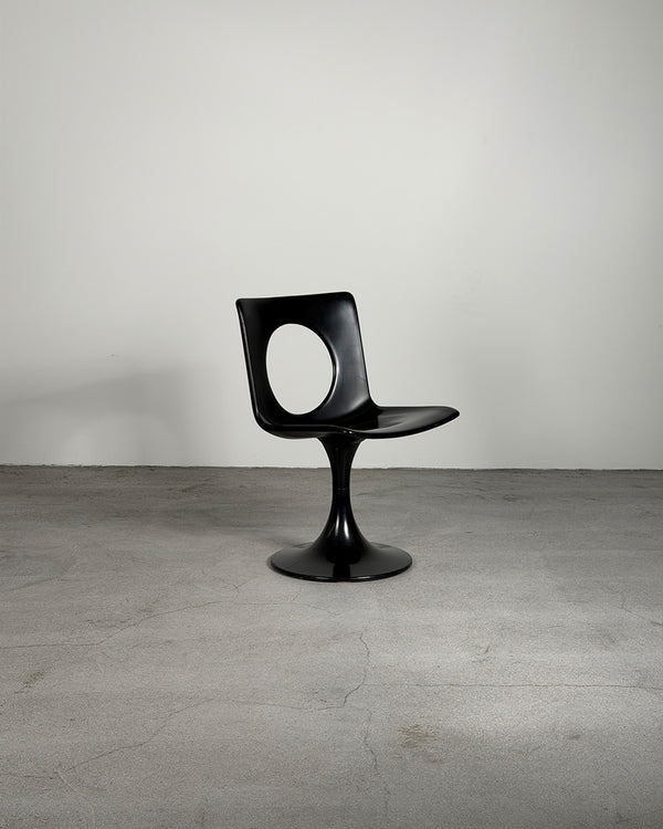 Black chair on a gray floor with a plain white wall background