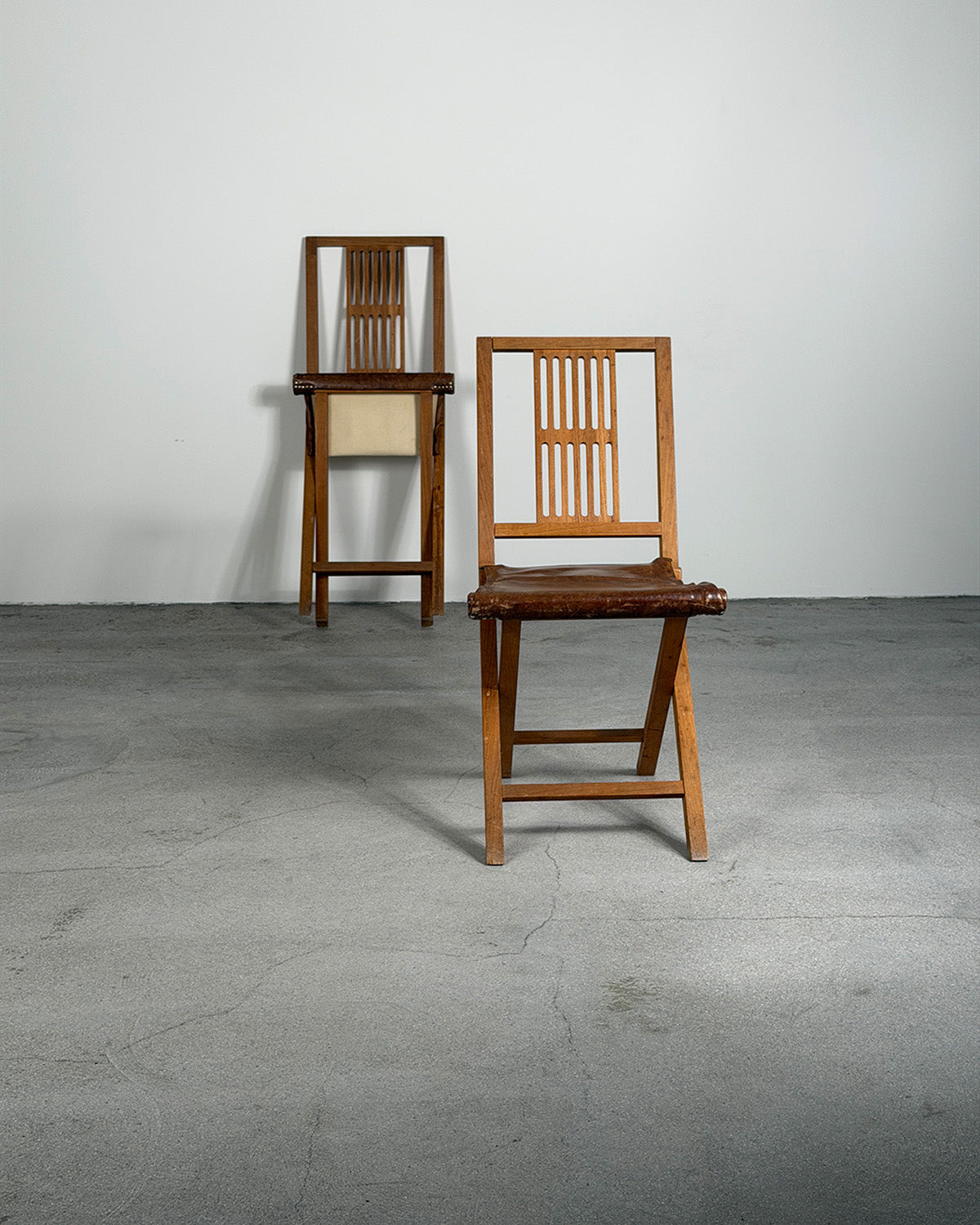 Two wooden chairs on a gray floor with a white wall background