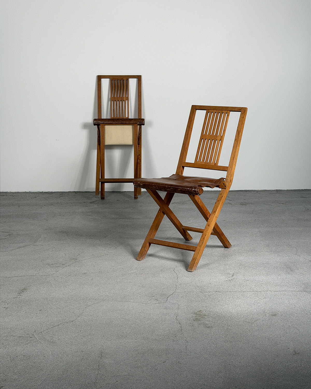 Two wooden folding chairs on a gray floor with a white wall background