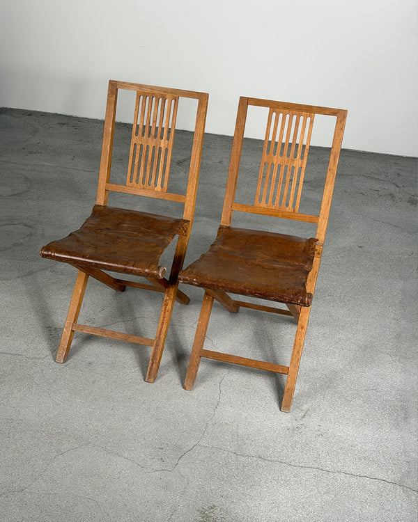 Two wooden chairs with leather seats on a gray floor.