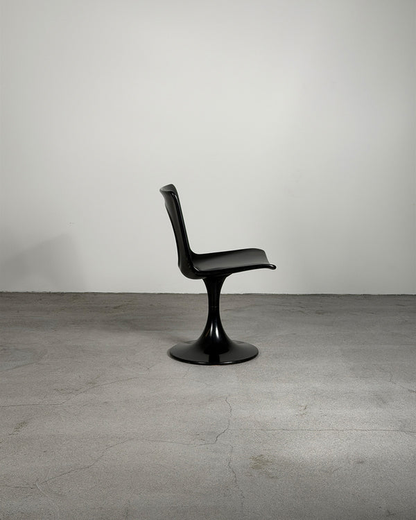 Black chair on a gray floor with a plain white wall background