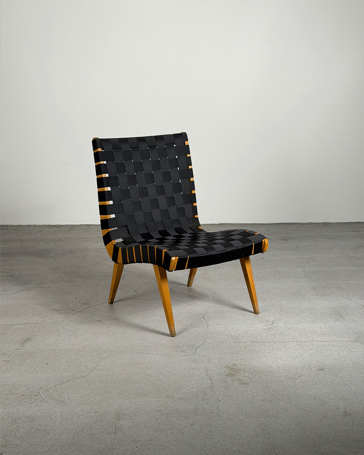 Modern Vostra 654W Lounge chair with black woven backrest and wooden legs on a gray floor.