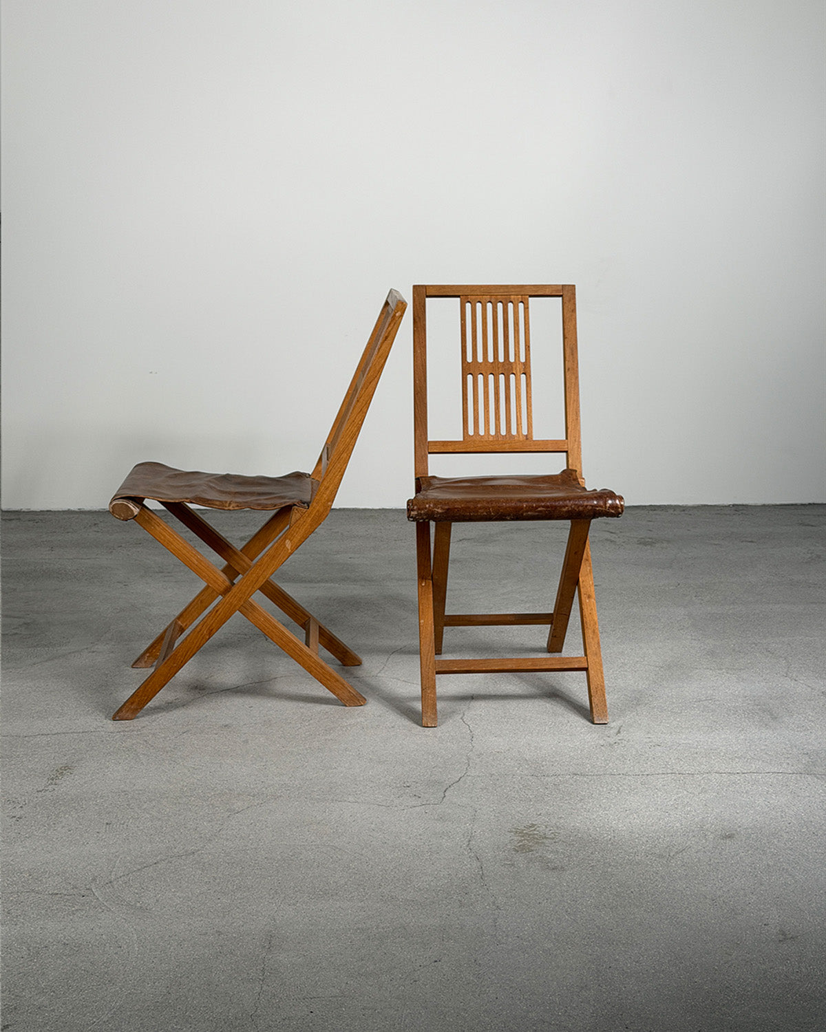 Two wooden folding chairs on a gray floor with a white wall background