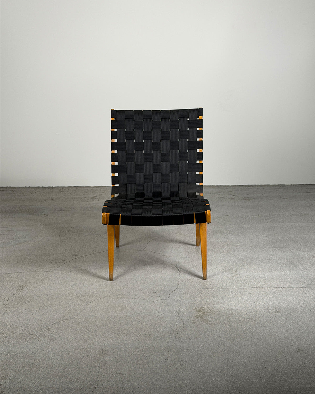 Black woven chair with wooden legs on a gray floor and white wall