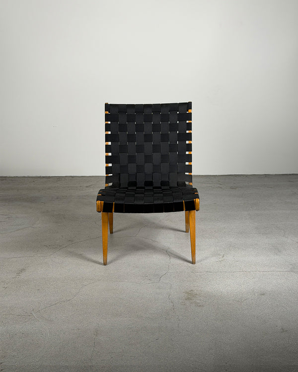 Black woven chair with wooden legs on a gray floor and white wall